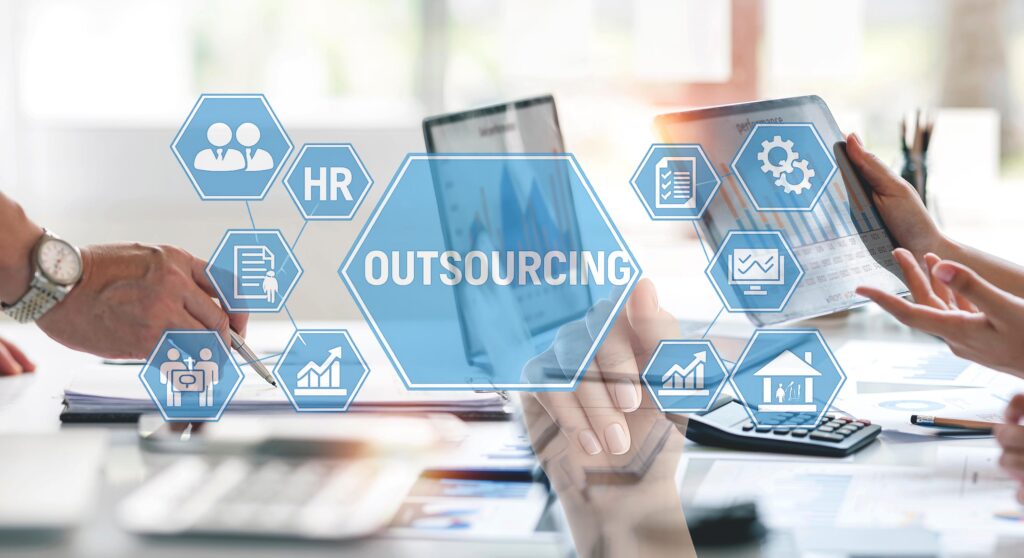 Concept for outsourcing payroll and hr services showing large icon with the word OUTSOURCING surrounded by smaller hr icons superimposed over computers and peoples hands making gestures.