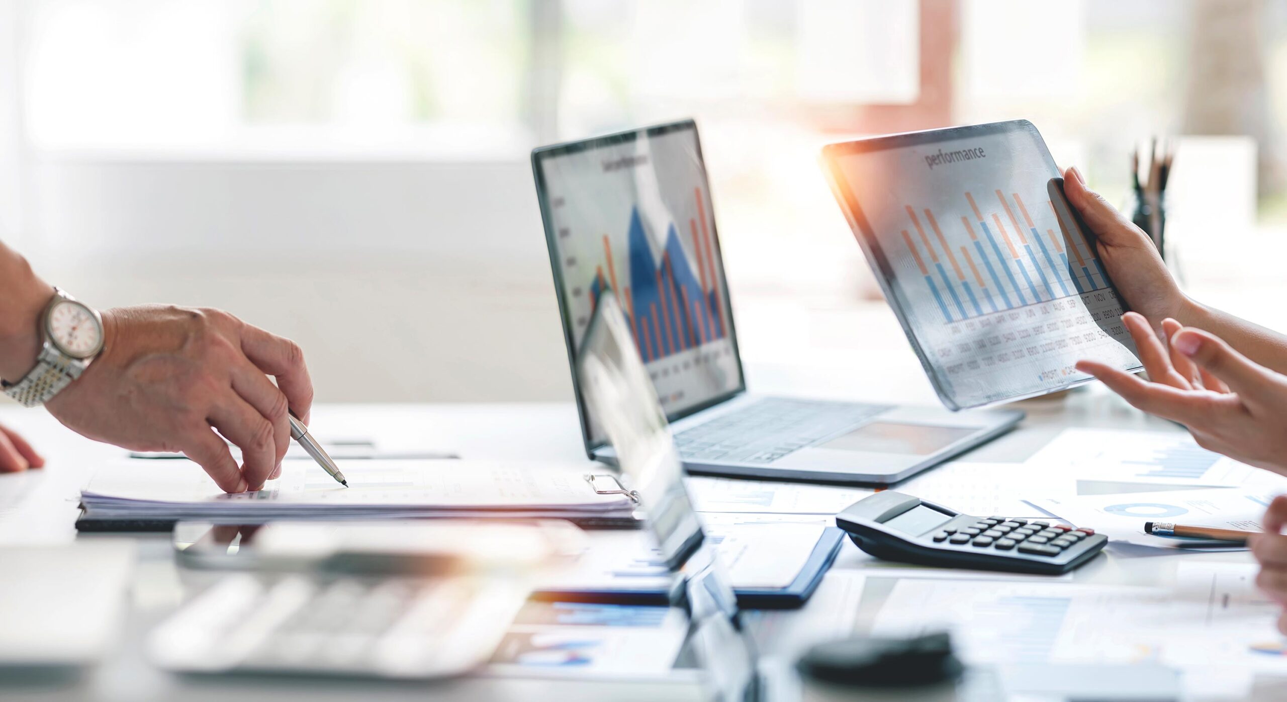 Photo of 2 computers and 1 tablet showing hands computing HR and payroll services for a business hands